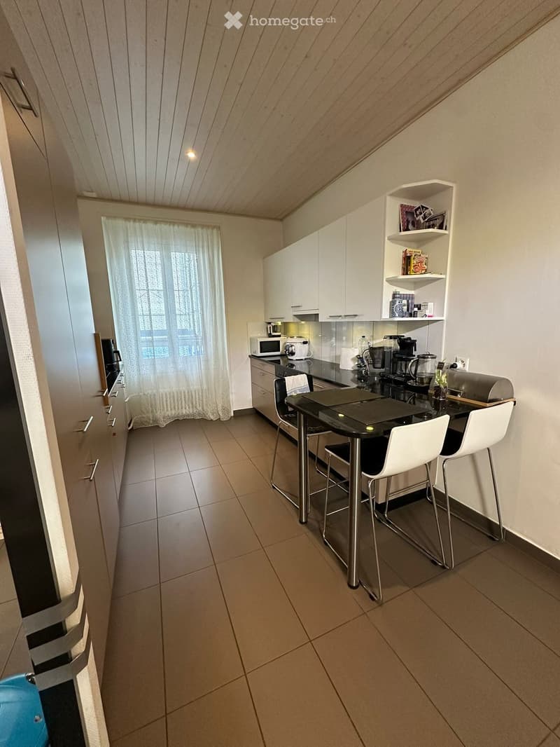 Modern kitchen with white cabinets, stainless steel appliances, a black dining table with two white chairs, and a microwave on the counter.
