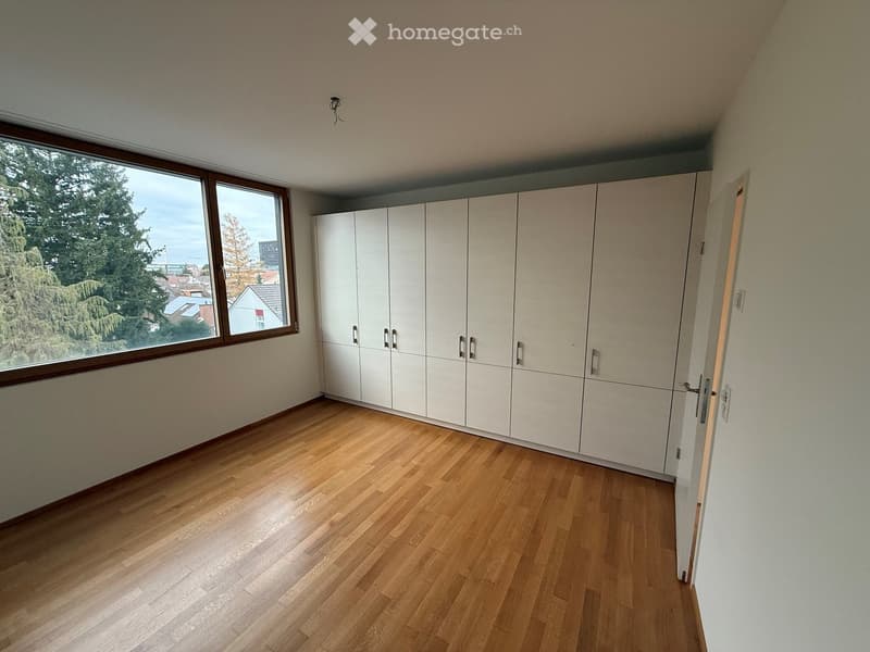 Empty room with wooden floor, large window, white walls, white cabinets