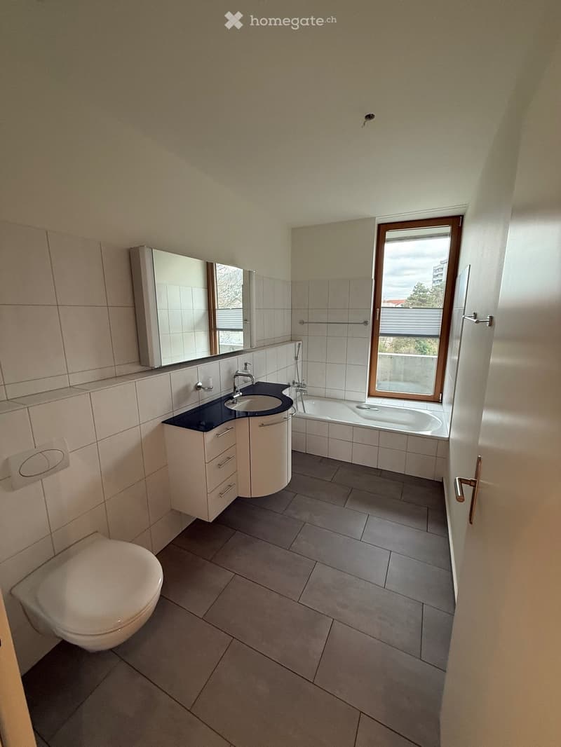 modern bathroom with white tiles, bathtub, sink, toilet, mirror, window