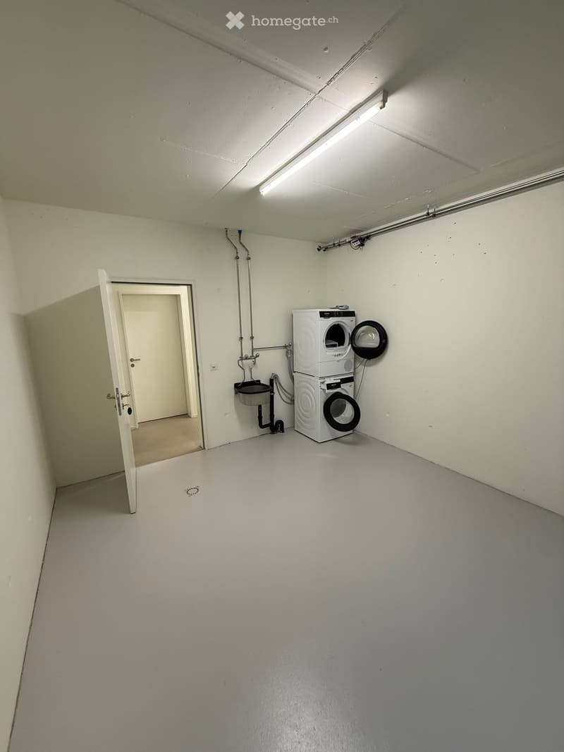 Empty room with white walls, white floor, a door, a sink, and two stacked washing machines.