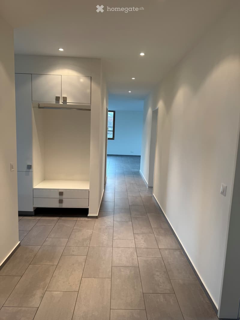 Empty hallway with white walls, tiled floor, built-in wardrobe with drawers, and a window at the end.