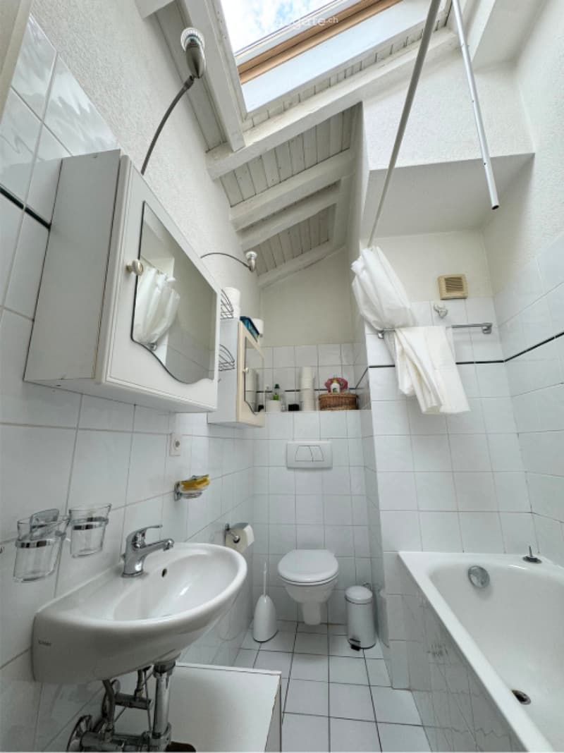 Bathroom with white tiles, sink, mirror, toilet, and bathtub. Shower curtain and towel are hanging on the rack.
