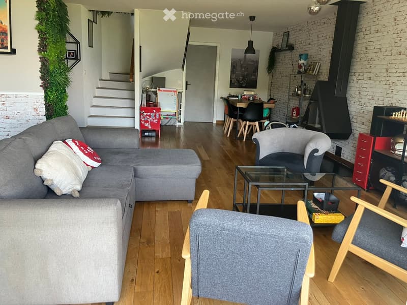 Furnished Room. A living room with a gray sofa, a coffee table, and a side table. There are chairs and a dining table with chairs. A bookshelf and a chest of drawers are on the right side. A plant and a poster are on the wall. A fan and a storage box are