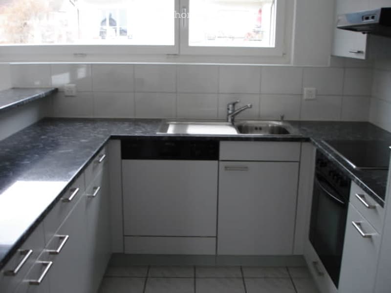 Tiled floor, white cabinets, granite countertop, stainless steel sink, built-in dishwasher, built-in washing machine, double oven, and a window