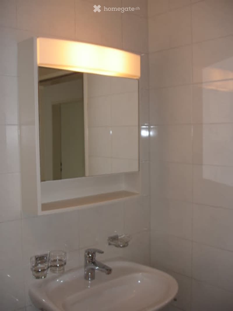 Bathroom with white tiled walls, under-mounted sink, mounted mirror, and vanity light above the mirror