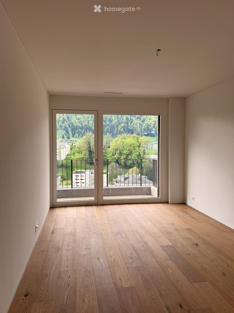 Empty room with large sliding glass doors leading to a balcony, wooden floors, and a view of a valley and mountains.