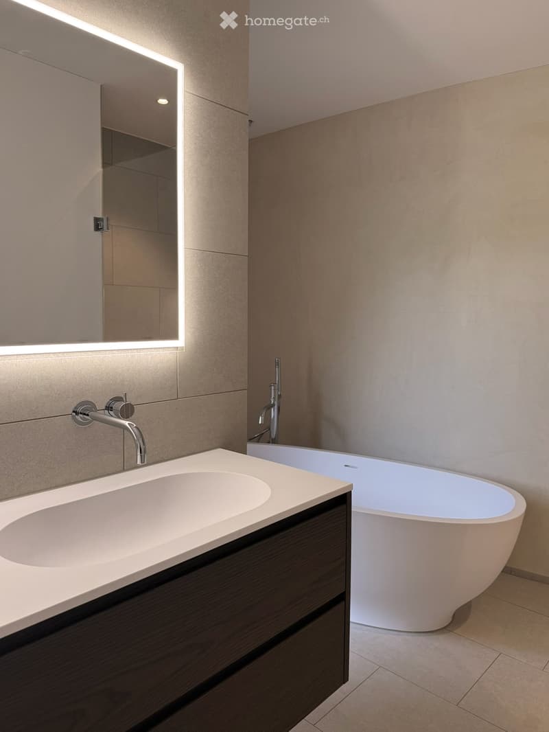 Modern bathroom with a white bathtub, a white sink, a mirror with a light, and a wooden cabinet.