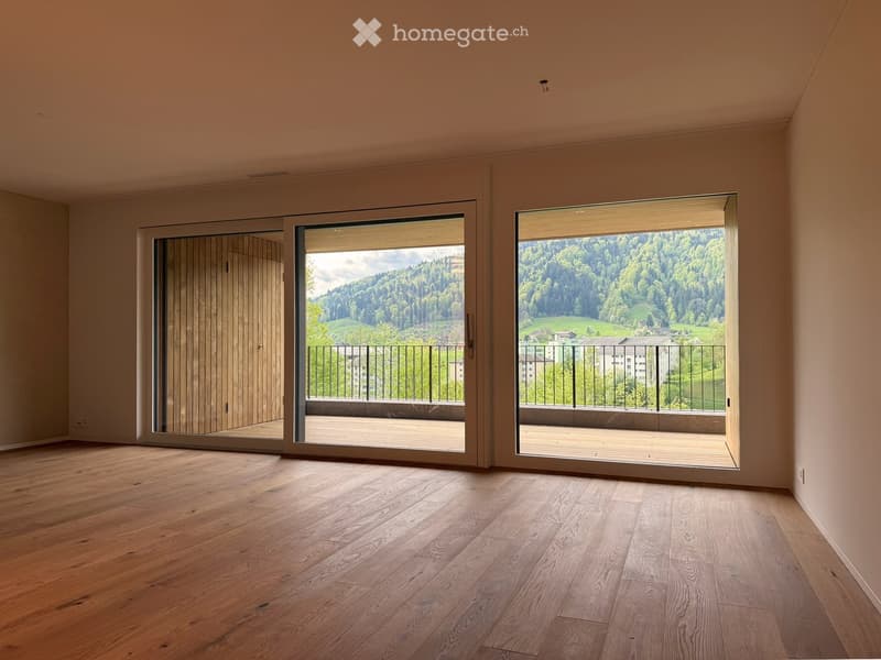 Empty room with wooden floors, large sliding glass doors leading to a balcony with a view of the mountains.