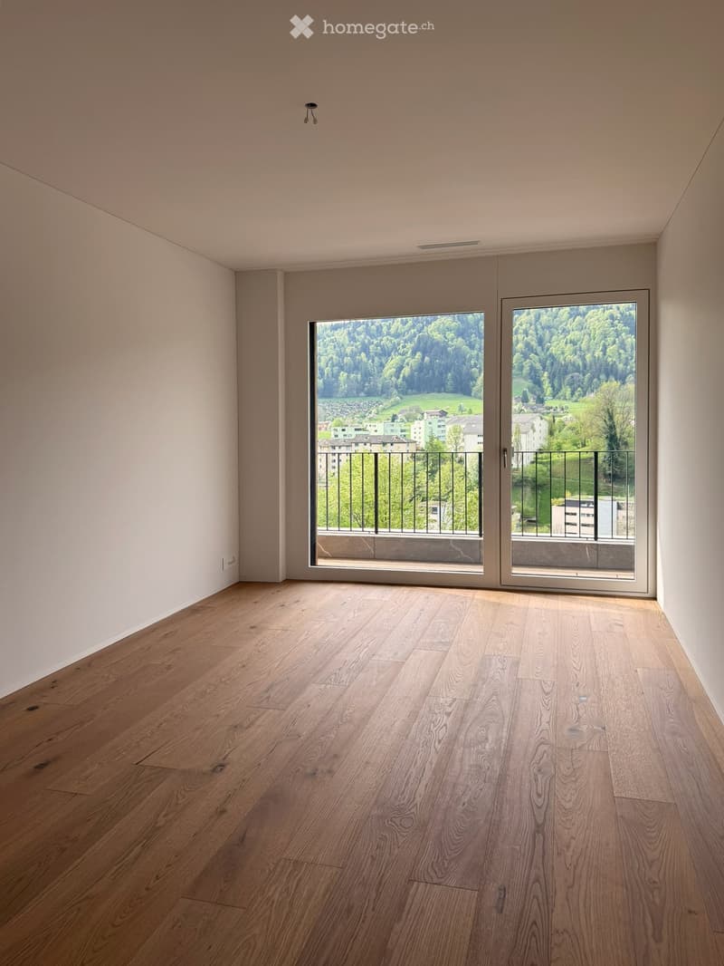 Empty room with hardwood floors, white walls, and large sliding glass doors leading to a balcony with a view of the mountains.