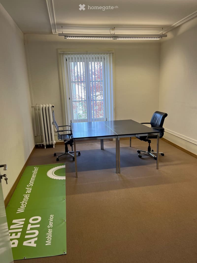 An empty office room with a desk, two chairs, a radiator, and a banner on the floor.