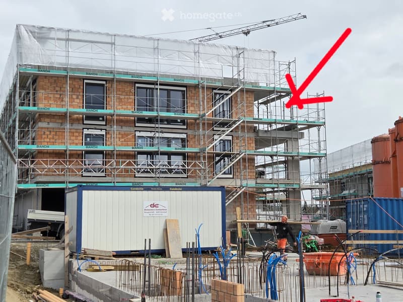 A multi-story building under construction with brick walls, glass windows, and scaffolding. A red arrow points to the right side of the building.