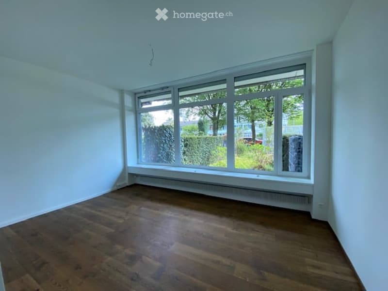 Empty room with white walls, wooden floor, large windows, and a white ceiling.