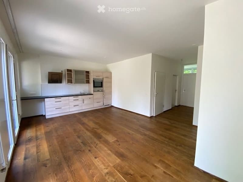 Empty kitchen with wooden floor, white walls, kitchen cabinets, microwave, sink, and windows