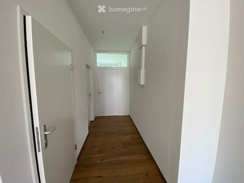 Empty hallway with wooden floor, white walls, two doors, and a skylight