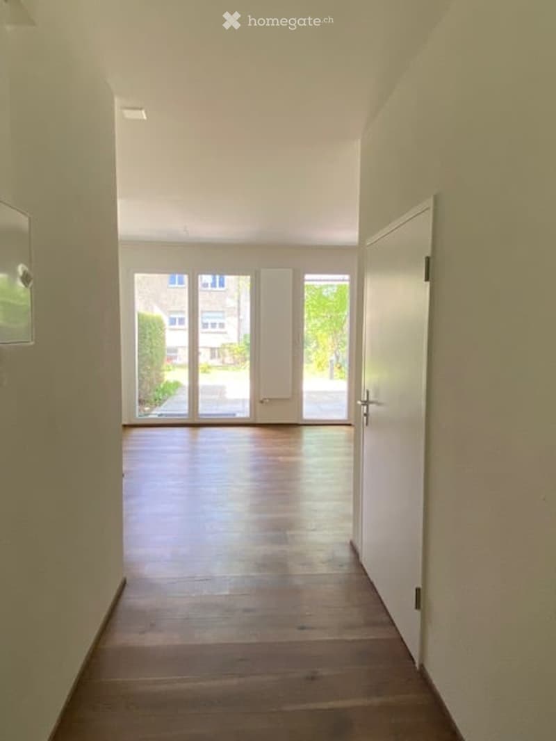 Empty hallway with wooden floor, white walls, sliding glass doors, and a white door.
