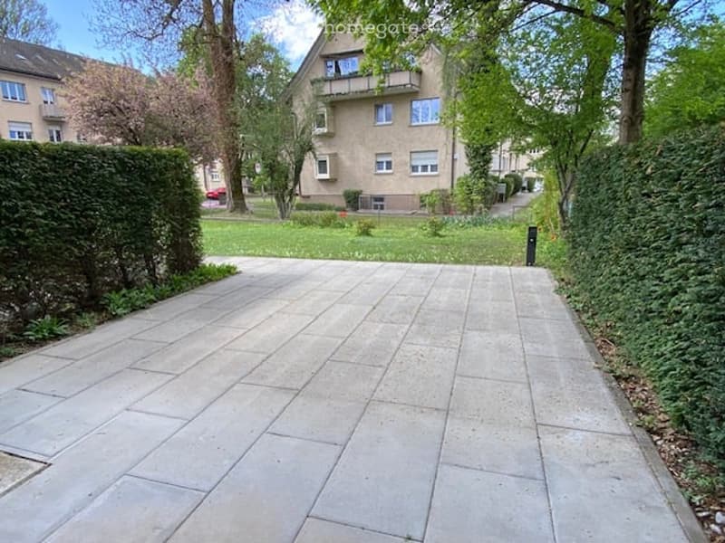 concrete pathway, hedges, trees, grass, building in the background