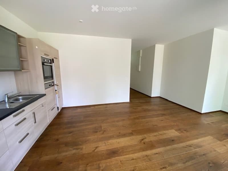 Empty kitchen with wooden floor, white walls, cabinets, sink, oven, and microwave
