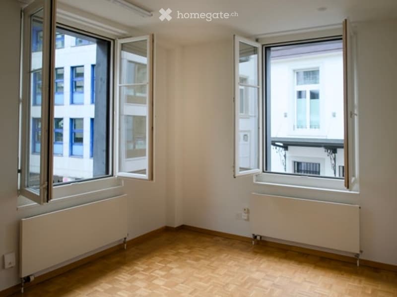 Empty room with wooden floors, white walls, and two large windows. There are two white radiators on either side of the room.