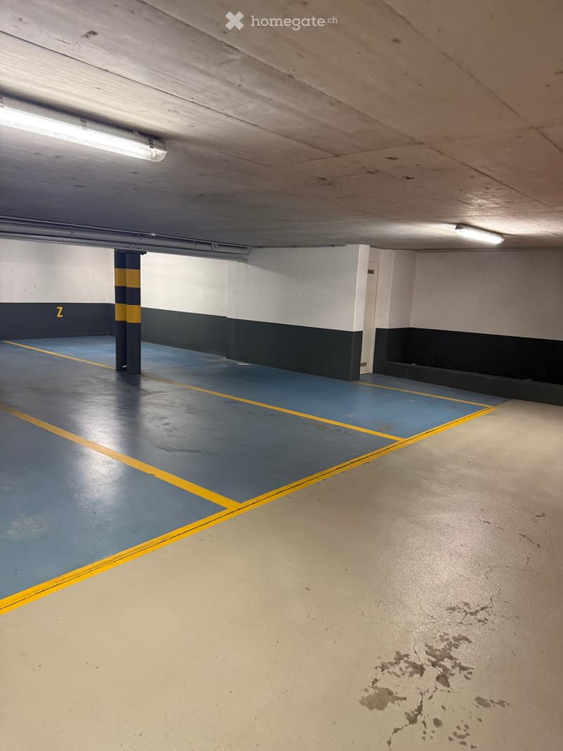 Unfurnished Room. Empty underground parking space with blue and yellow markings, white walls, and a ceiling with fluorescent lights.