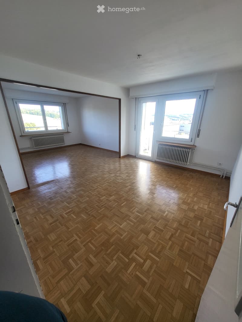Empty room with wooden herringbone flooring, white walls, large windows, and radiators.
