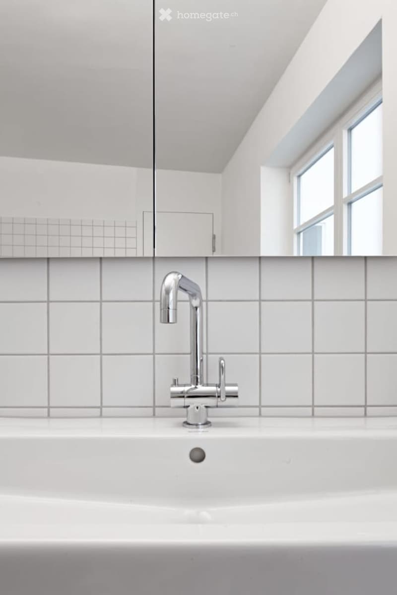 Bathroom with white tiles, a white sink, and a silver faucet.