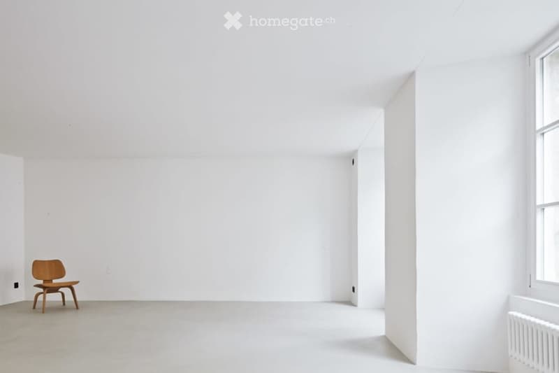Completely empty room with white walls, ceiling, and floor. A wooden chair and a white radiator are present.