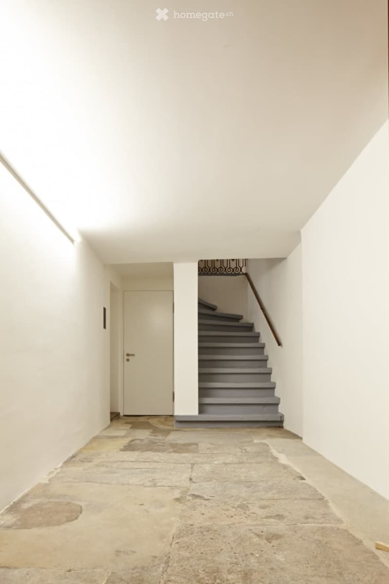 Empty corridor with white walls, a door, and a staircase leading to the upper floor.