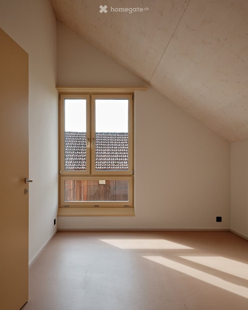 Empty room with white walls, wooden floor, and a window with a view of a tiled roof.