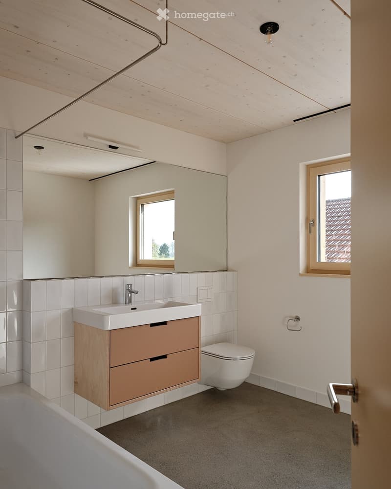 Modern bathroom with white tiles, a large mirror, a white sink, a wooden cabinet, and a white toilet.