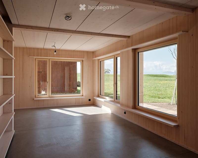An empty room with wooden walls and floor, featuring large windows and built-in wooden benches.