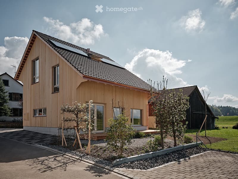 Modern house with wooden exterior, solar panels on the roof, and a driveway.