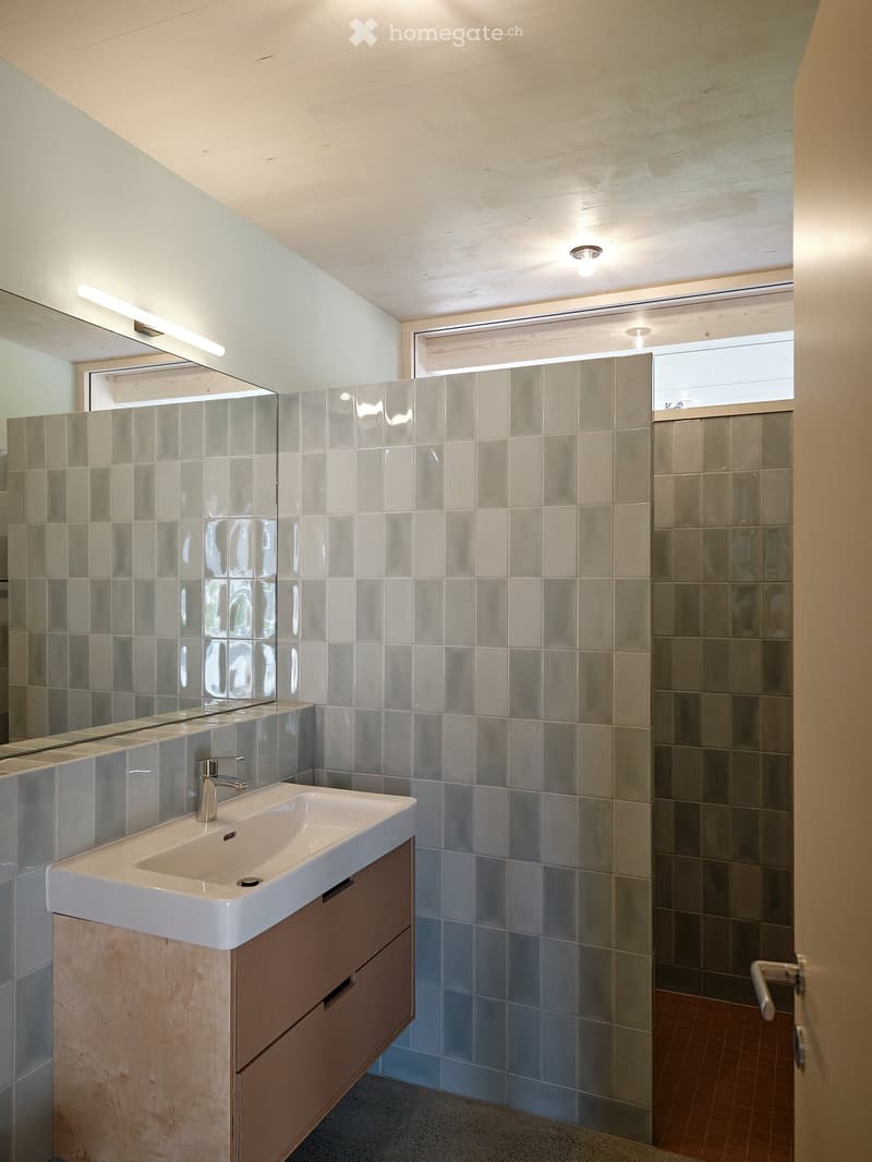 Bathroom with tiled walls, a white sink, a mirror, and a wooden cabinet with drawers.
