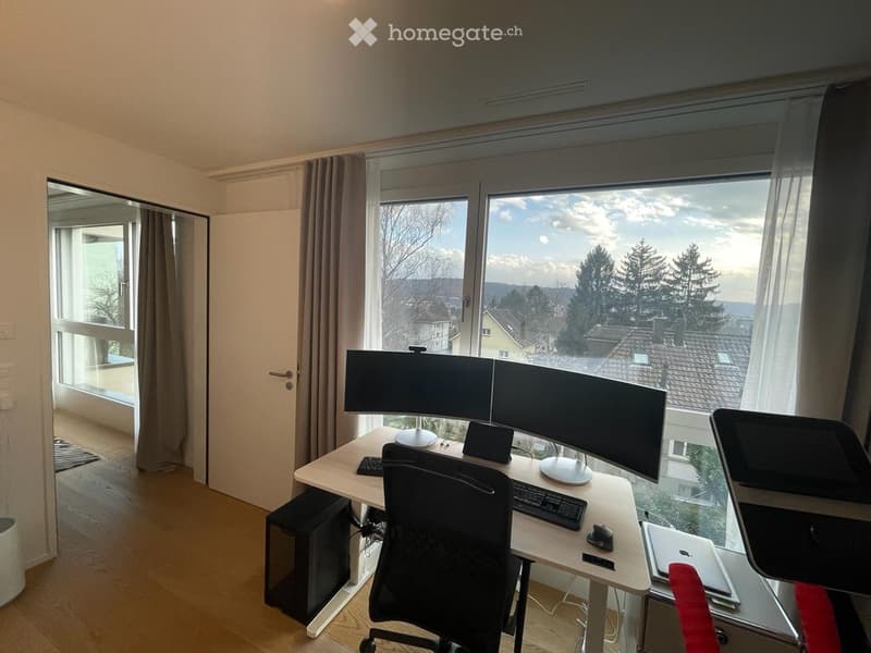 desk with 3 monitors, black chair, wooden floor, large window with view