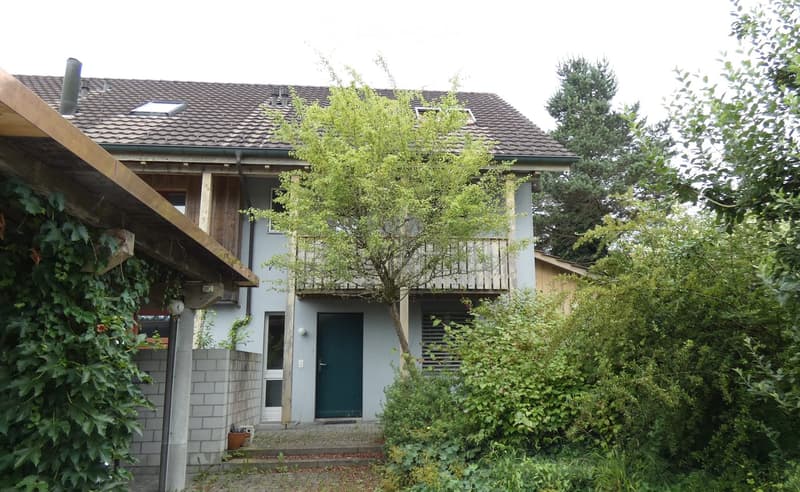 2 story house, brown roof, balcony, white walls, green door, surrounded by plants