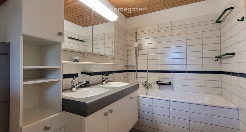 Bathroom with white tiles, double sink, bathtub, mirror, wooden ceiling, and a shelf