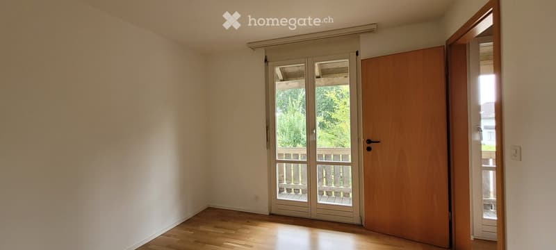 Empty room with wooden flooring, white walls, and a sliding glass door leading to a balcony.