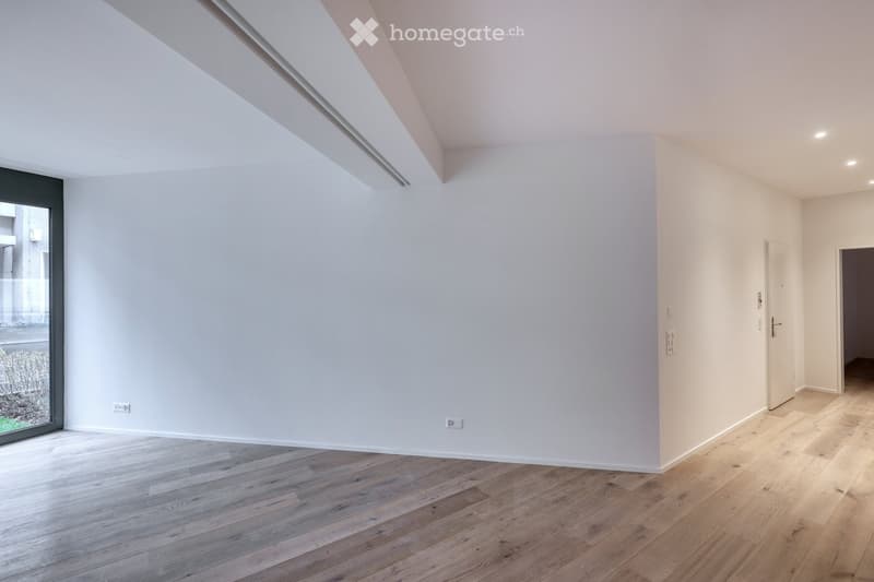 An empty room with white walls, wooden floor, and glass door. There are power outlets on the walls.