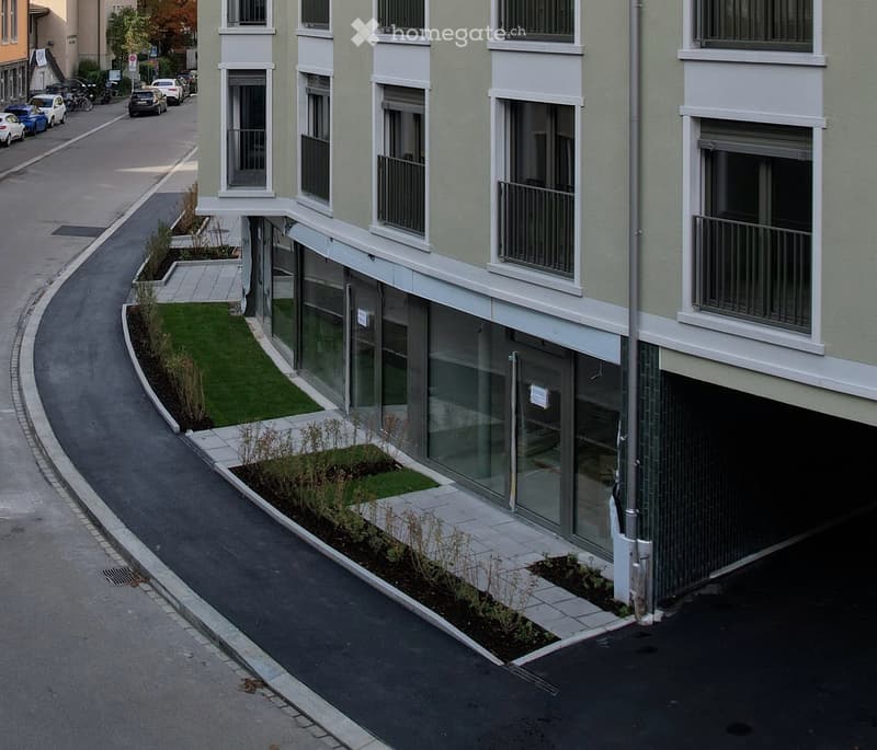 Modern building with glass windows and balconies, surrounded by a landscaped area with grass and plants.