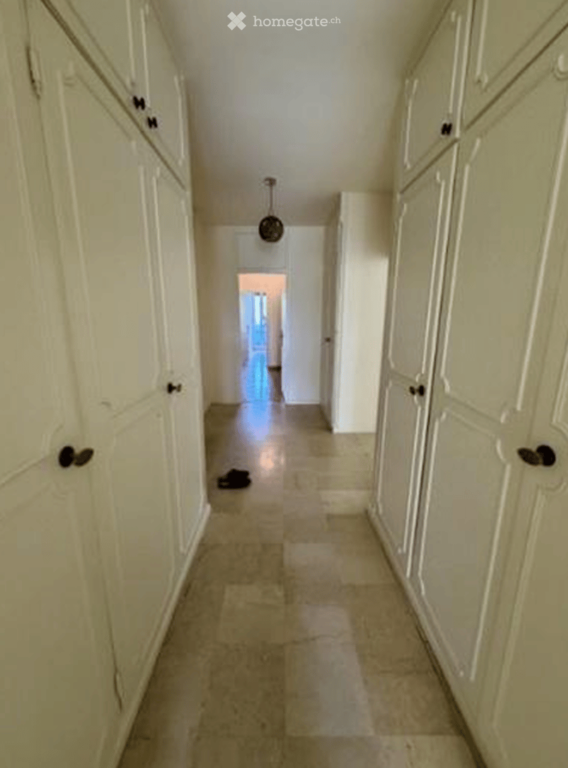 Empty hallway with tiled floor, white cabinets, and a hanging lamp.