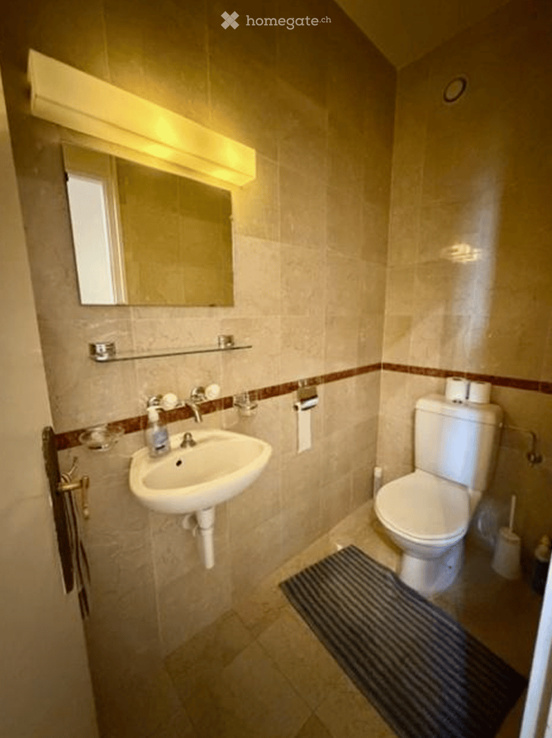Bathroom with tiled walls, white sink, mirror, and toilet. A towel is hanging on the rack.
