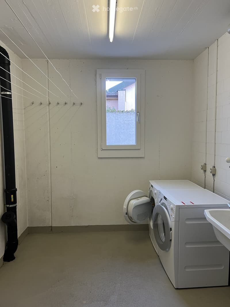 A small laundry room with a washing machine, clothes drying rack, and sink.