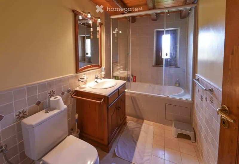 Bathroom. Bathroom with a toilet, sink, mirror, bathtub, and step stool. The walls are tiled, and there is a towel on the floor.