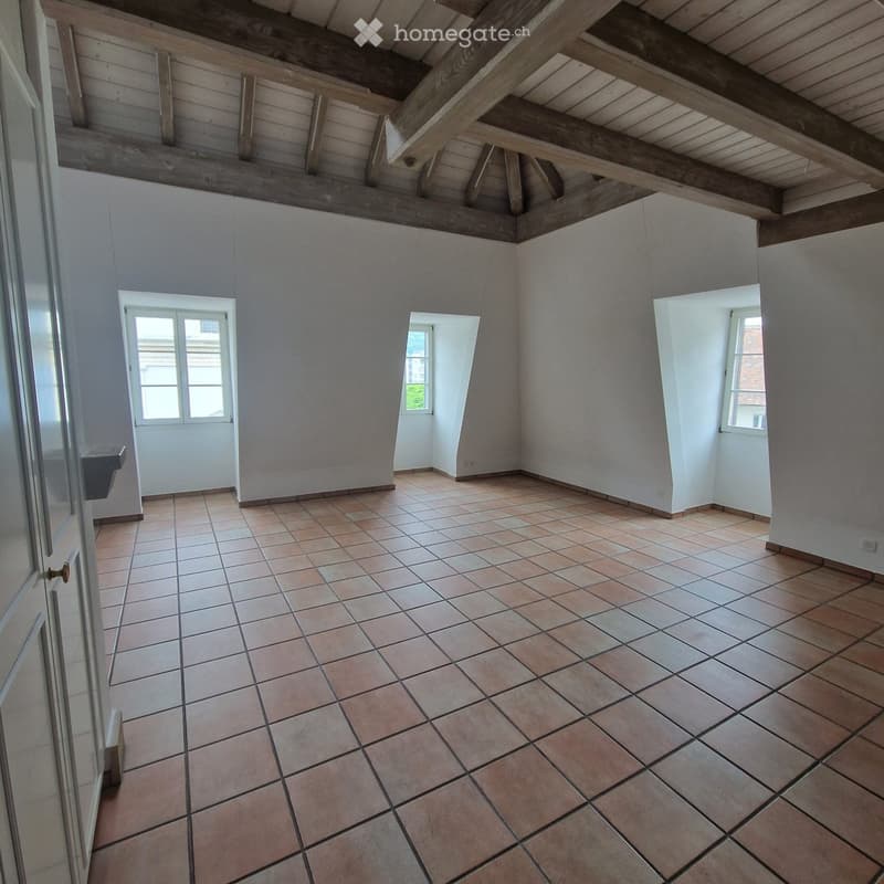 Empty room with exposed wooden ceiling, tiled floor, white walls, three windows