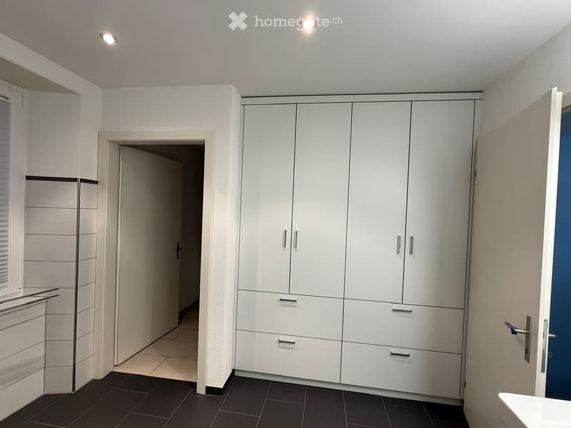 Empty room with white walls, black tiled floor, large white wardrobe, white door, white sink, white window with blinds