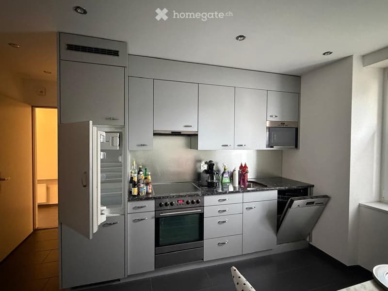modern kitchen with white cabinets, black countertops, stainless steel appliances, open refrigerator, dishwasher, oven, microwave, sink, bottles on the counter