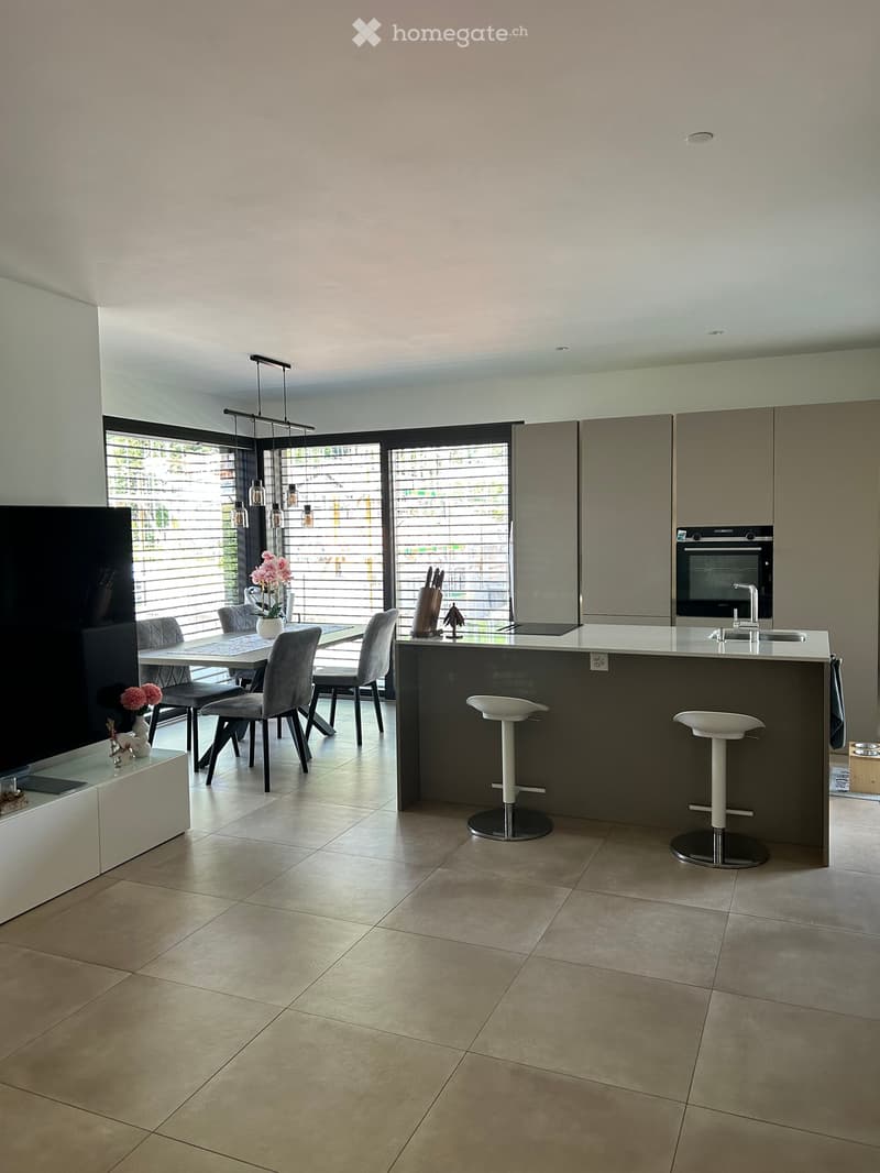 Modern kitchen with a dining area, large windows, and a central island with bar stools.