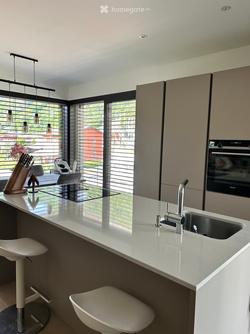 Modern kitchen with a large island, white countertops, stainless steel sink, and a built-in oven and dishwasher.