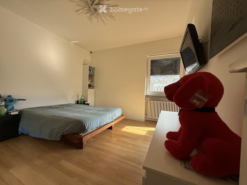 Bedroom. Bedroom with wooden bed, blue bedspread, nightstand, and a red stuffed animal on a shelf. A white radiator and a mounted TV are also present.