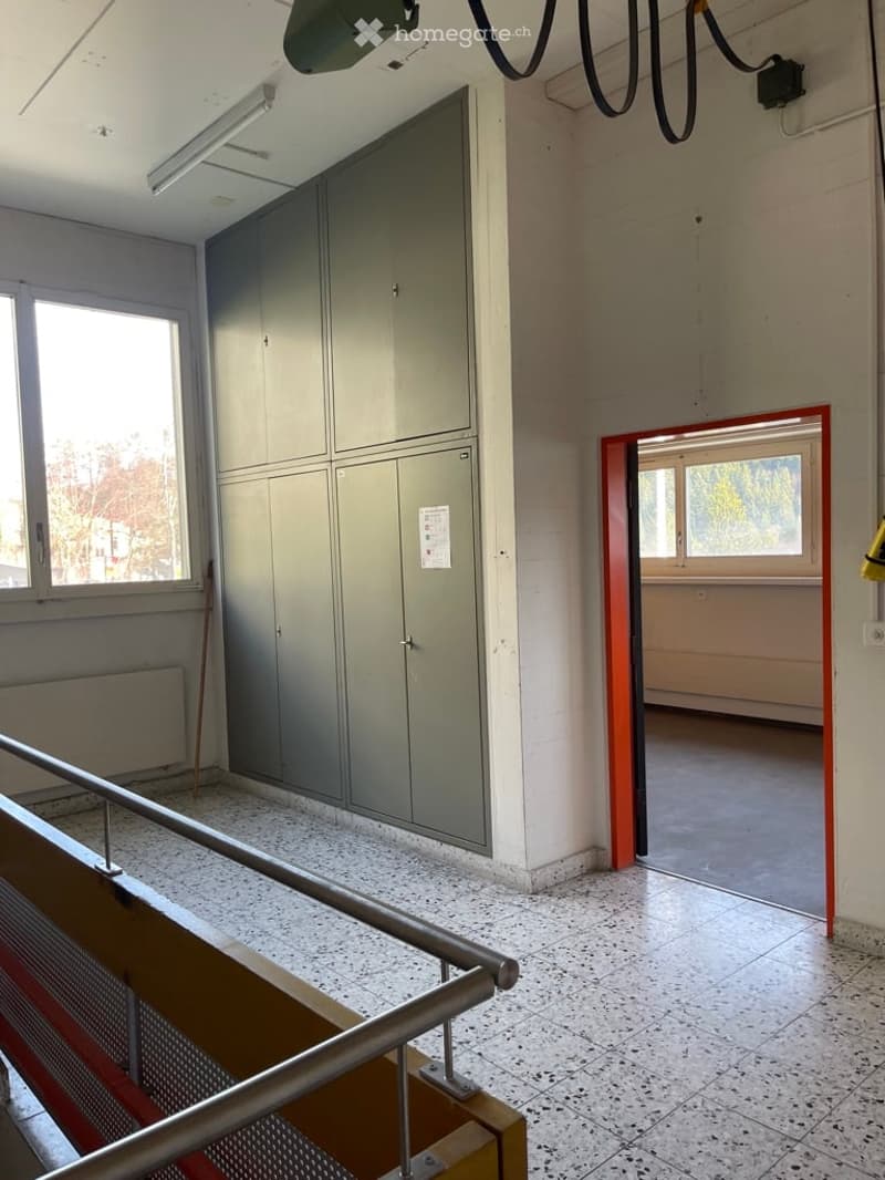 Open store room with large built-in storage units, windows, white tiled floor, metal handrail.