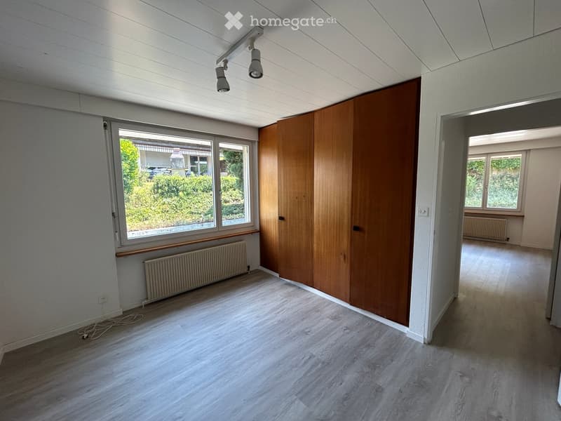 Empty room with wooden flooring, white walls, large windows, and a wooden closet. No furniture or equipment present.